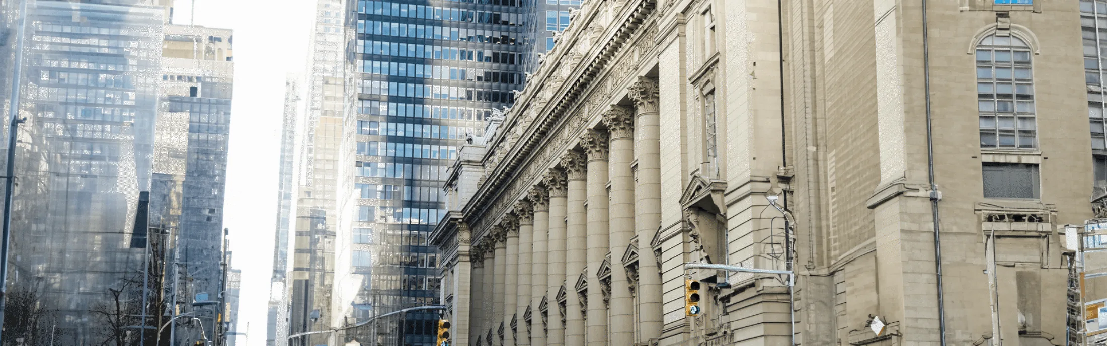 Street view of a historic building with tall columns alongside modern glass skyscrapers in an urban cityscape.
