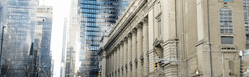 Street view of a historic building with tall columns alongside modern glass skyscrapers in an urban cityscape.
