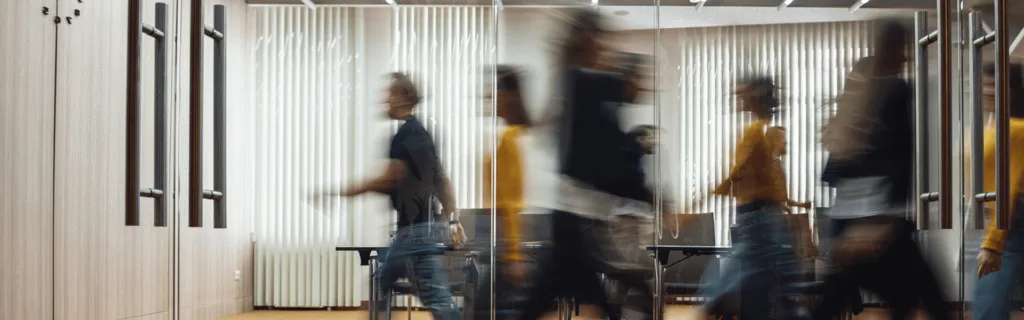 Blurred motion of people walking in an office hallway, reflecting a busy and dynamic work environment.
