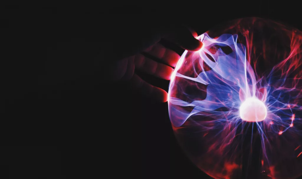 Hand reaching towards a glowing plasma ball with vibrant blue and red electric arcs radiating from the center in a dark background.